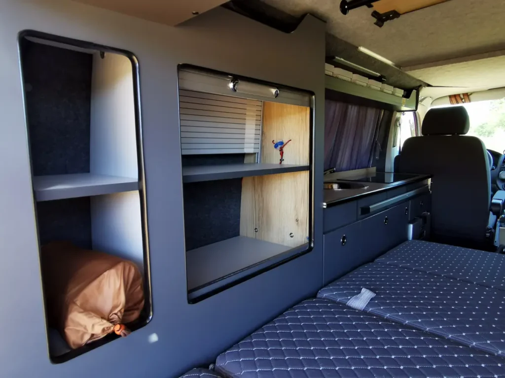 Detailansicht eines modernen Campervan-Innenraums mit Stauraum, Küchenzeile und komfortabler Schlaffläche.