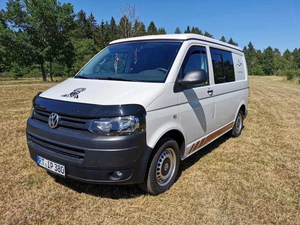 Weißer Volkswagen Campervan für Vanlife mit Streifen-Dekor auf sonniger Wiese.