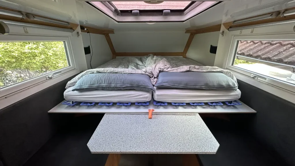 Gemütlicher Selbstausbau-Innenraum mit Betten, Tisch und Fenstern in einem Campervan.