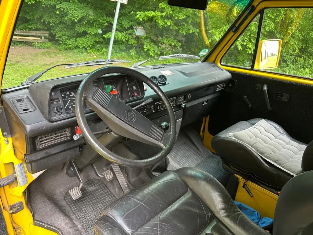 Innenansicht eines gelben klassischen Campervans mit Lenkrad, Armaturenbrett und schwarzen Ledersitzen.