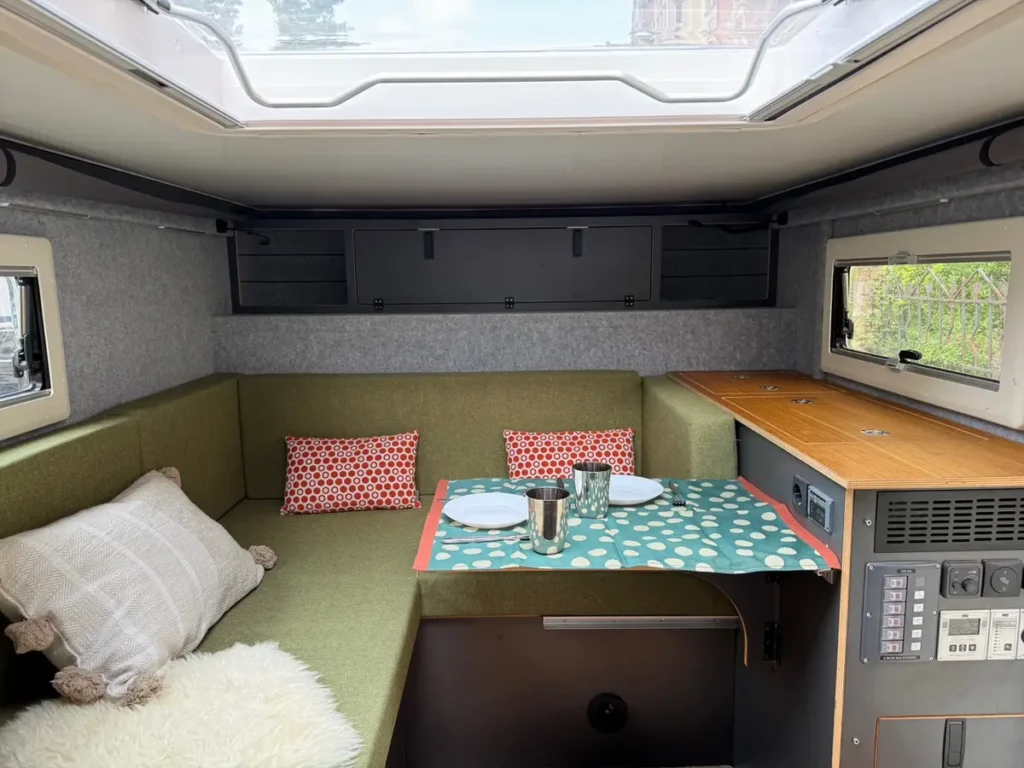 Gemütlicher Selbstausbau-Innenraum eines Campervans mit Sitzbereich, Klapptisch und Küchenzeile.