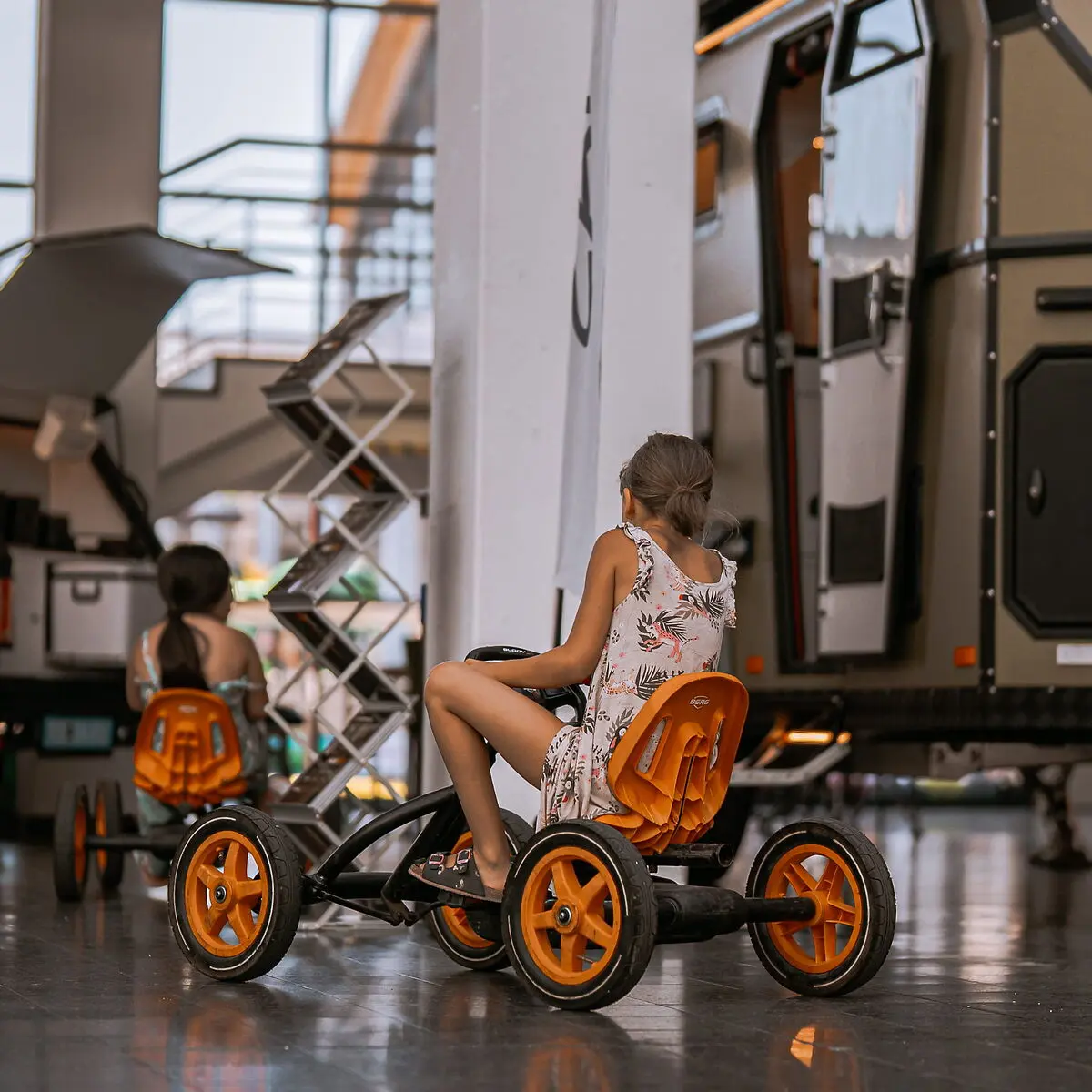 Zwei Kinder fahren Go-Karts vor einem großen Expeditionsmobil mit offener Tür.